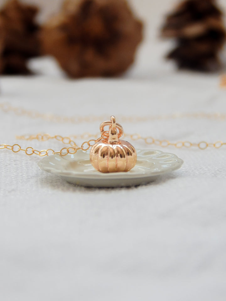 Close-up of gold pumpkin charm necklace on a decorative plate.