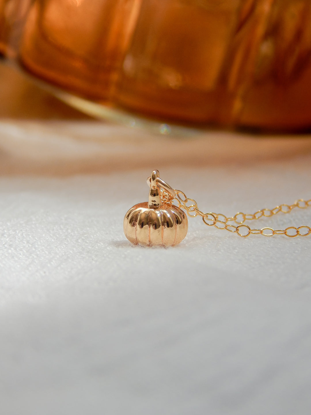 Gold pumpkin charm necklace with a warm, golden background.