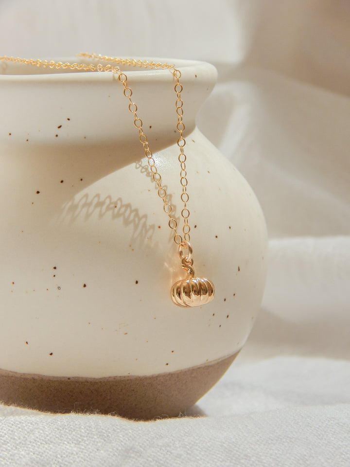 Gold pumpkin charm necklace hanging elegantly on a ceramic vase.