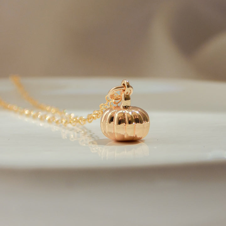 Gold pumpkin charm necklace displayed on a white surface.