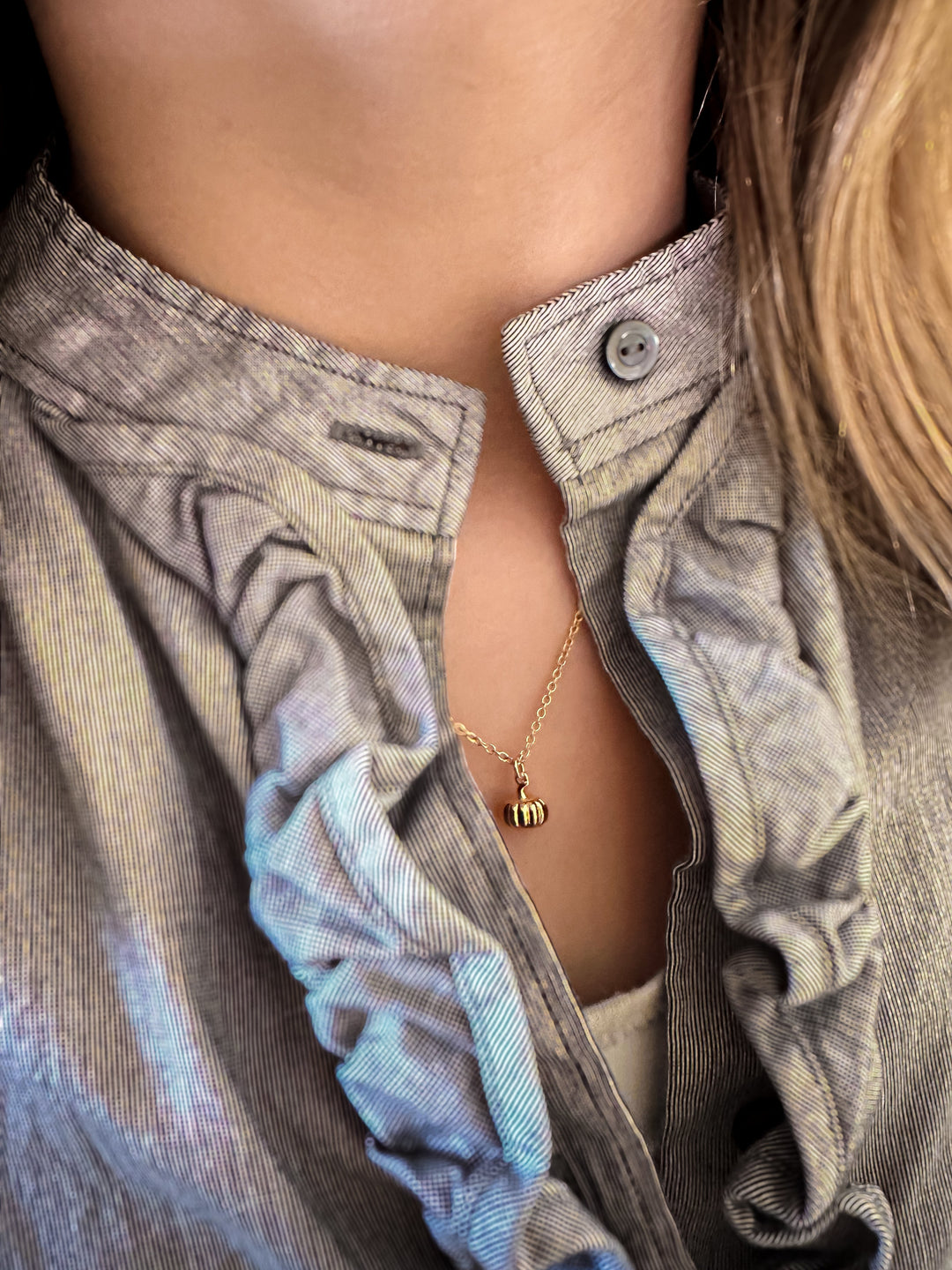 Gold pumpkin charm necklace worn with a ruffled gray blouse.